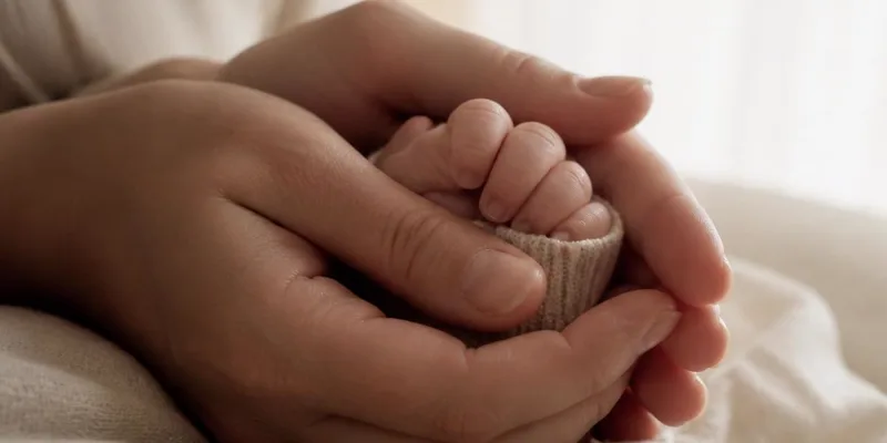 Mãos de uma mãe acolhendo a mão de um recém-nascido sobre um tecido claro